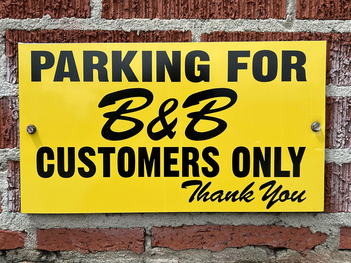 Yellow parking sign reading Parking for B and B Customers Only mounted on brick wall in West Asheville