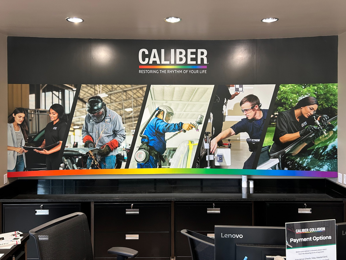 Caliber Collision large full-color interior wall display with photographs of collision repair technicians in Asheville North Carolina