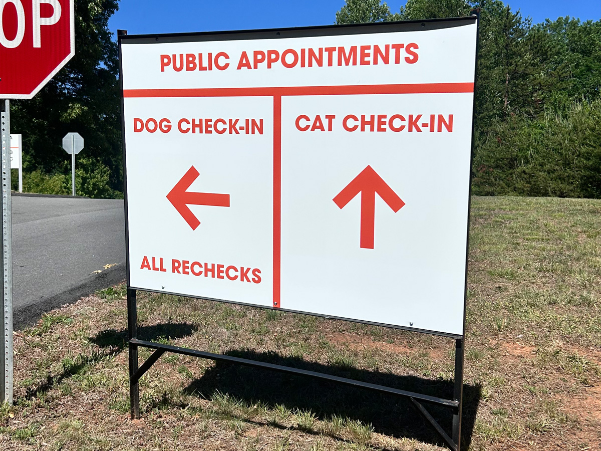 Veterinary directional yard sign showing dog check-in and cat check-in directions